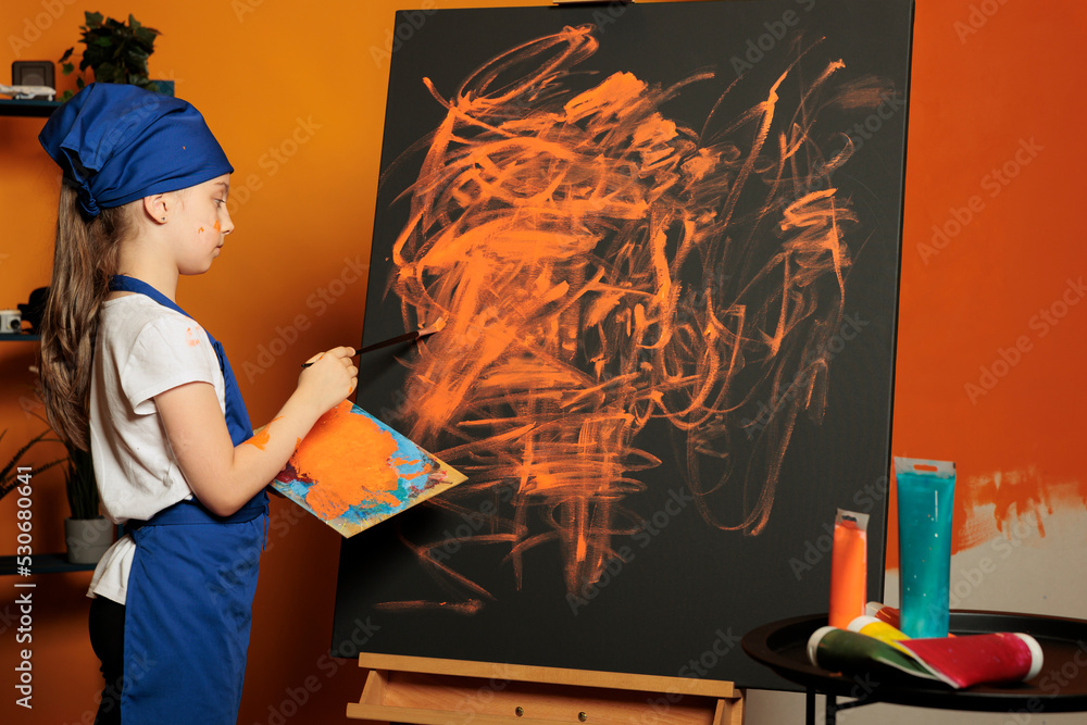 Small girl using orange paint color on canvas, creating artwork