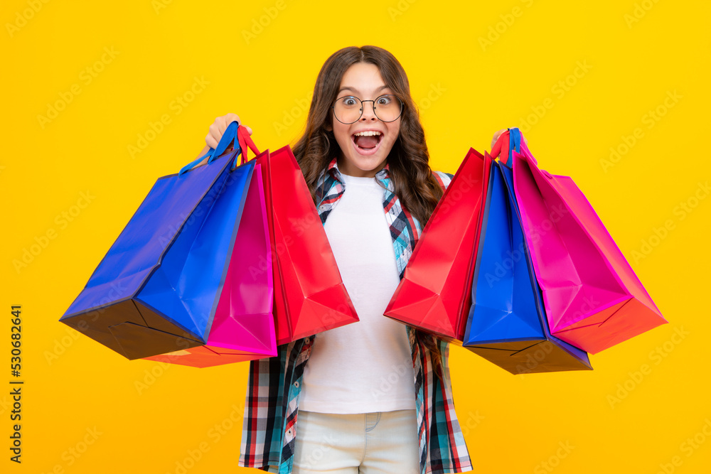 Amazed teen girl. Child girl hold shopping bag enjoying sale isolated on yellow background. Portrait of teenager girl is ready to go shopping. Excited expression, cheerful and glad.