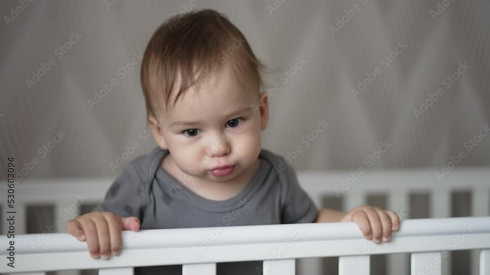 Sweet little baby boy making faces standing in his crib. Lovely ten-month old child being active after sleep. Close up. Sweet little baby boy making faces standing in his crib. Lovely ten-month old child being active after sleep. Close up.