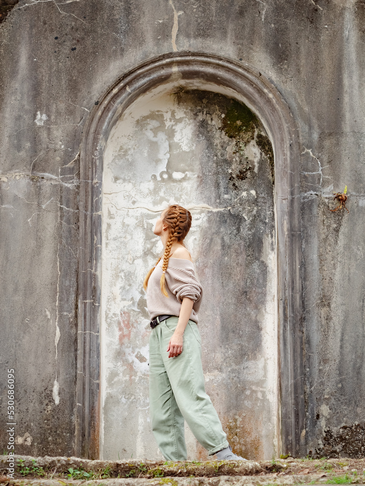 Obraz premium Woman in arch of ancient architecture outdoors. Arched stone stucco structure of ancient architecture. Tourist walk through abandoned places