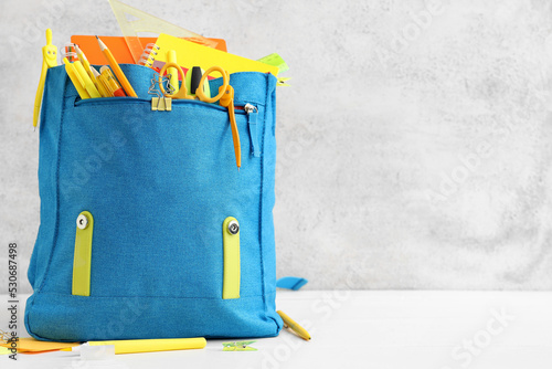 Blue backpack with school stationery on light background