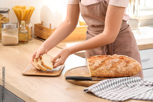 Woman putting slices of fresh bread onto board in kitchen, closeup