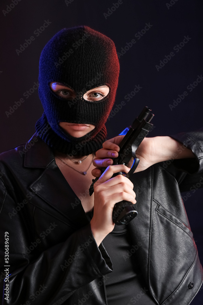 Young woman in balaclava and leather jacket holding gun against black background Young woman in balaclava and leather jacket holding gun against black background