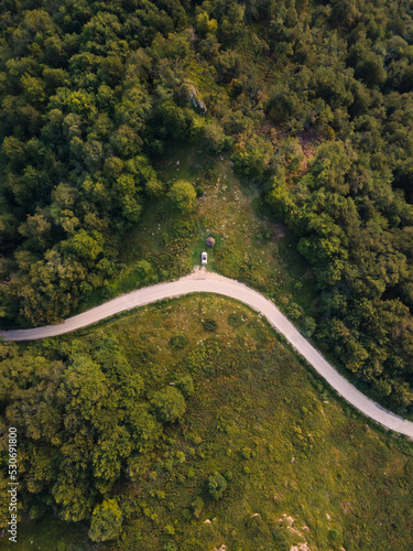 Top down aerial drone view of the road in mountain range trough the trees and forest and car parked wild travel rural vacation and nature concept background © Miljan Živković