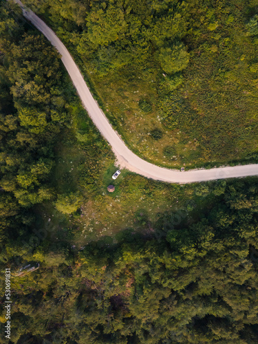 Top down aerial drone view of the road in mountain range trough the trees and forest and car parked wild travel rural vacation and nature concept background © Miljan Živković