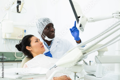 Attentive doctor dentist showing woman patient x-ray of teeth on computer