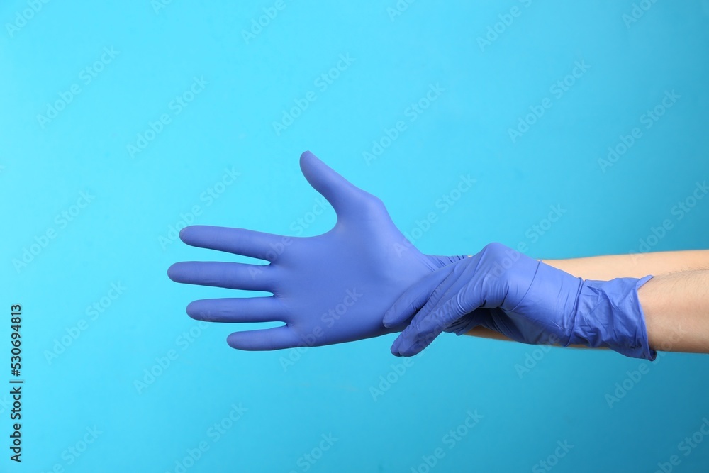 Person putting on medical gloves against light blue background, closeup of hands