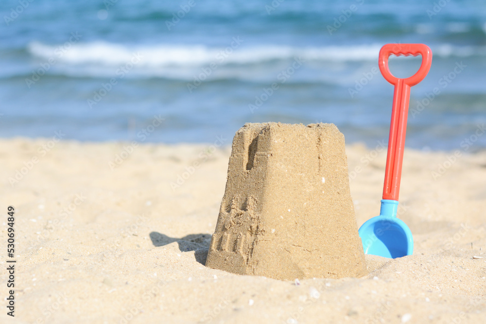 Beautiful sand castle and plastic shovel on beach near sea, space for text Beautiful sand castle and plastic shovel on beach near sea, space for text