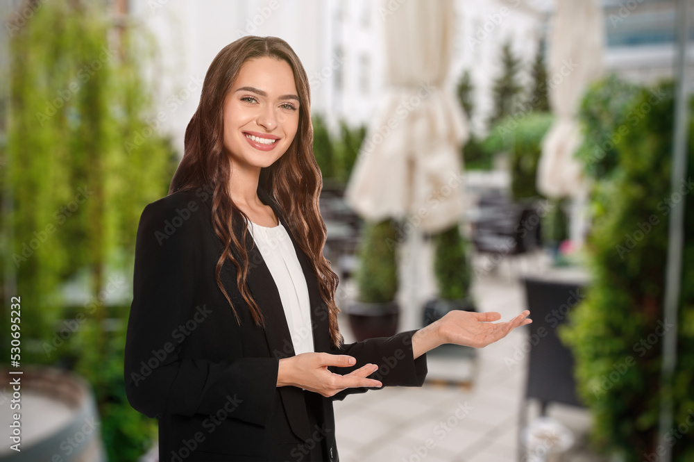 Portrait of hostess in uniform and blurred view of cafe on sunny day. Space for text Portrait of hostess in uniform and blurred view of cafe on sunny day. Space for text