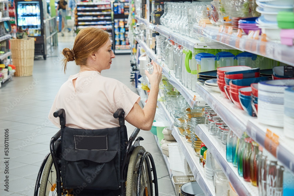 Obraz premium back view of a woman choosing goods in a supermarket, sitting in a wheelchair