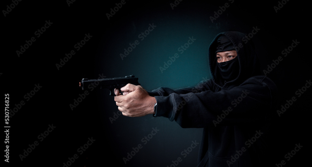 Rubbery or thief man wearing black mask long black T-shirt he holding gun to make rubber dangerous man is a crime concept. Rubbery or thief man wearing black mask long black T-shirt he holding gun to make rubber dangerous man is a crime concept.