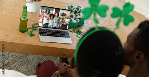 African american couple making st patrick's day video call to group of friends on laptop at home