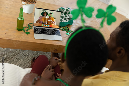 African american couple making st patrick's day video call to male friends on laptop at home