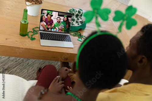 African american couple making st patrick's day video call to group of friends on laptop at home