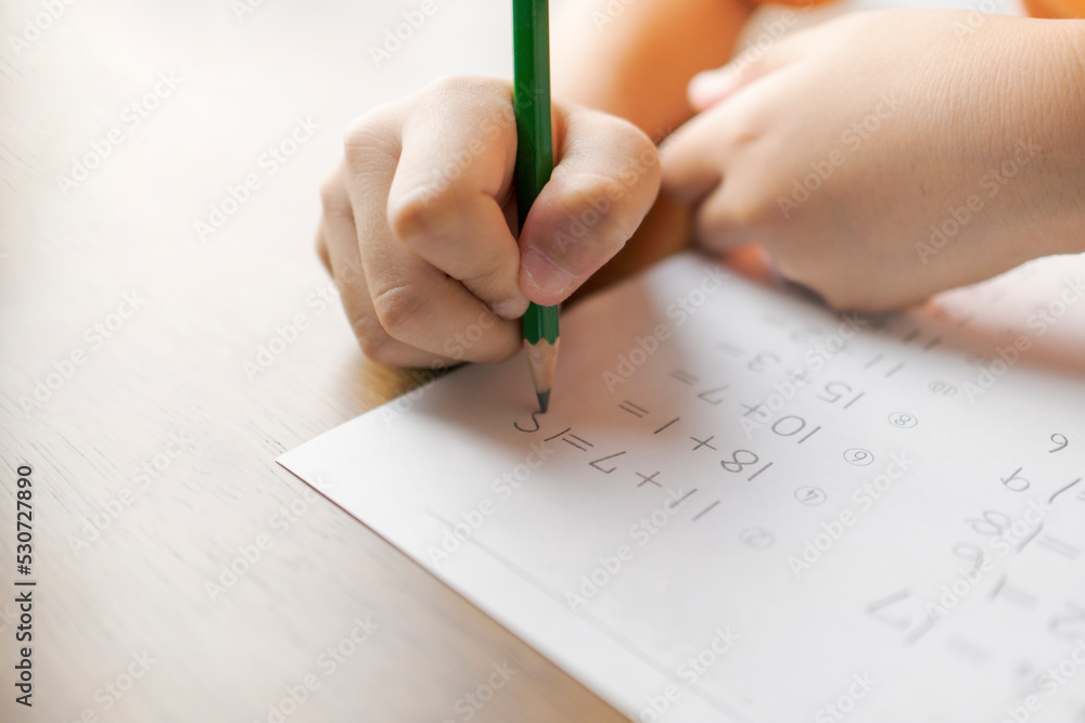 足し算の計算問題を解く一年生の子供の手。小学生、算数、宿題、プリント、勉強。 足し算の計算問題を解く一年生の子供の手。小学生、算数、宿題、プリント、勉強。
