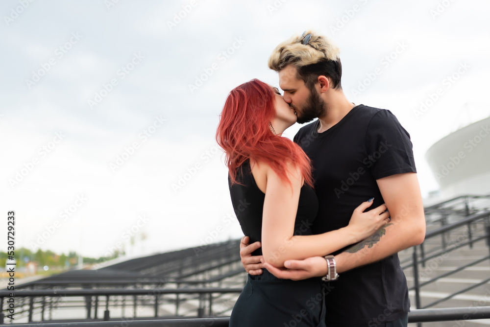 Stylish couple in love in black clothes walks in the park and hugs. Lovely couple of hipsters hugging and kissing on the background of the stairs. Youth, love and lifestyle concept