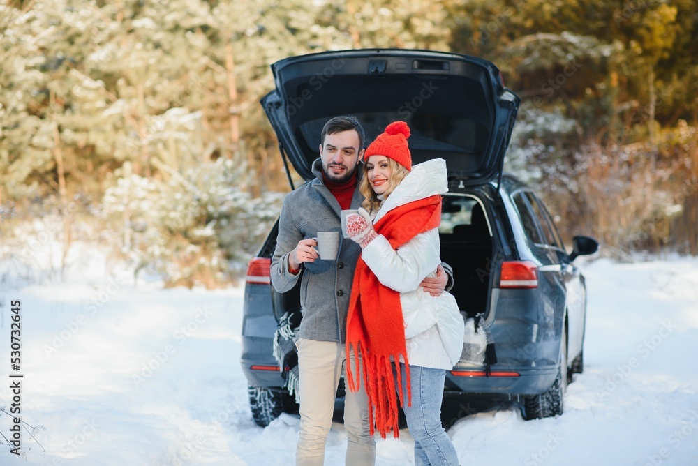 lovely smiling couple sitting in car trunk in winter forest