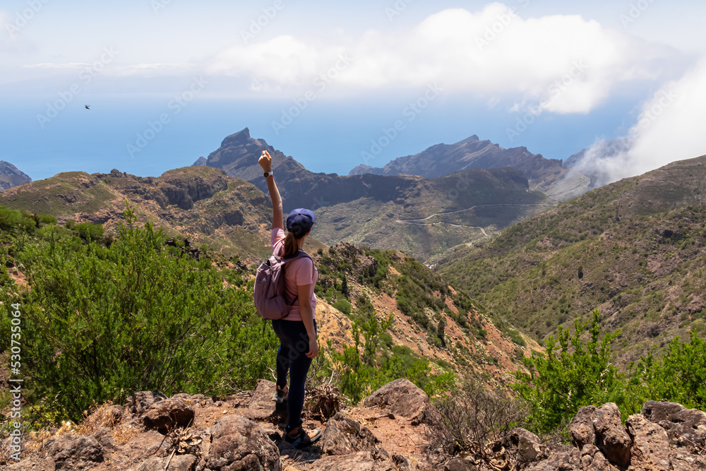 Woman with backpack enjoying panoramic view on the Teno mountain massif seen from summit Pico Verde, Tenerife, Canary Islands, Spain, Europe. Hiking trail between Masca and Santiago. Wanderlust vibe