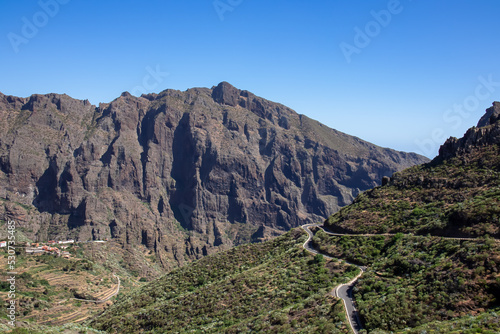 Aerial panoramic view on narrow winding curvy mountain road to remote village Masca, Teno mountain massif, Tenerife, Canary Islands, Spain, Europe. Massive steep rock formation Roque de la Fortaleza