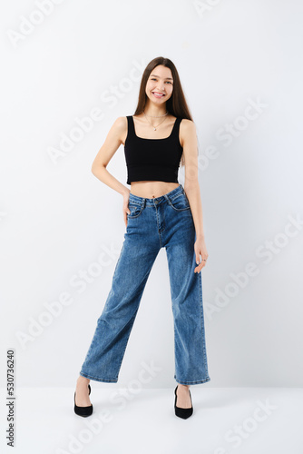 Portrait of laughing young woman in black tank top and wide jeans