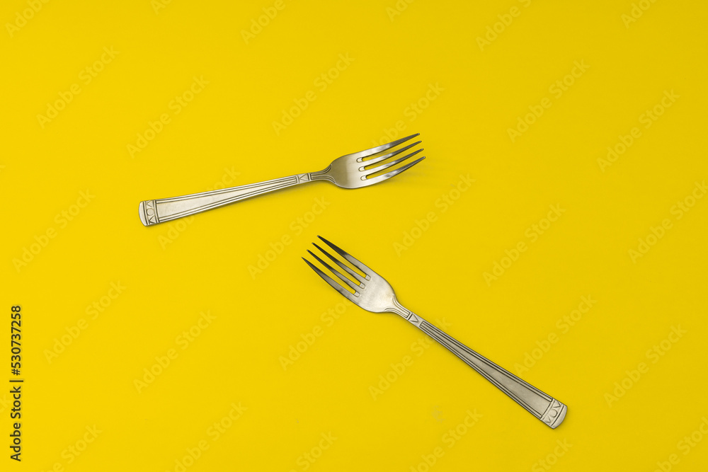 Silver forks lie on a yellow background, minimalism Silver forks lie on a yellow background, minimalism
