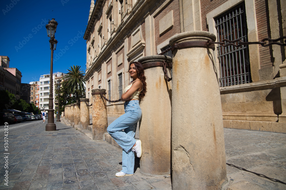 Beautiful young woman in casual clothes leaning on a column in the cathedral of Seville. The woman is on tourism enjoying her holidays in Spain. Travel concept.