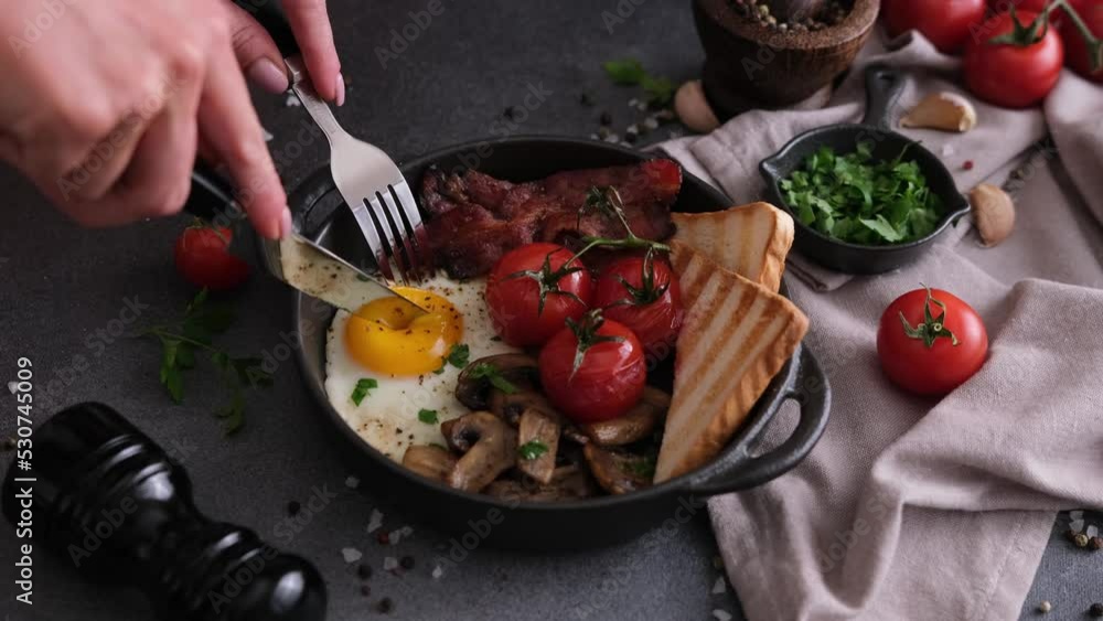 woman puts tasty dish breakfast onto dark background - fried bacon, eggs, mushrooms and tomatoes in ceramic pot woman puts tasty dish breakfast onto dark background - fried bacon, eggs, mushrooms and tomatoes in ceramic pot