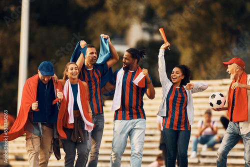 Картината върху платно Group of cheerful sports fans celebrating victory of their soccer team on the street