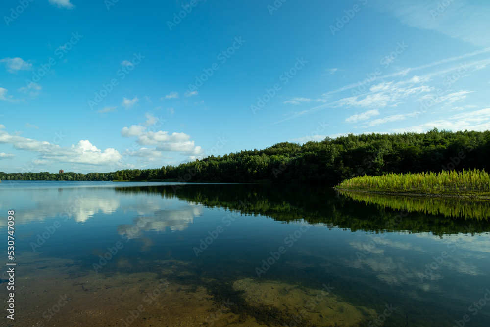 Reflection of trees in lake, blue skies with some small puffs of white clouds. Reflection of trees in lake, blue skies with some small puffs of white clouds.