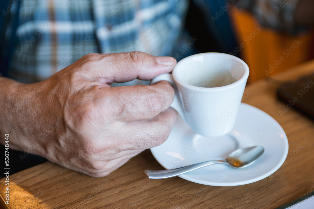Hands of old man holding cup of coffee on the wood table Hands of old man holding cup of coffee on the wood table