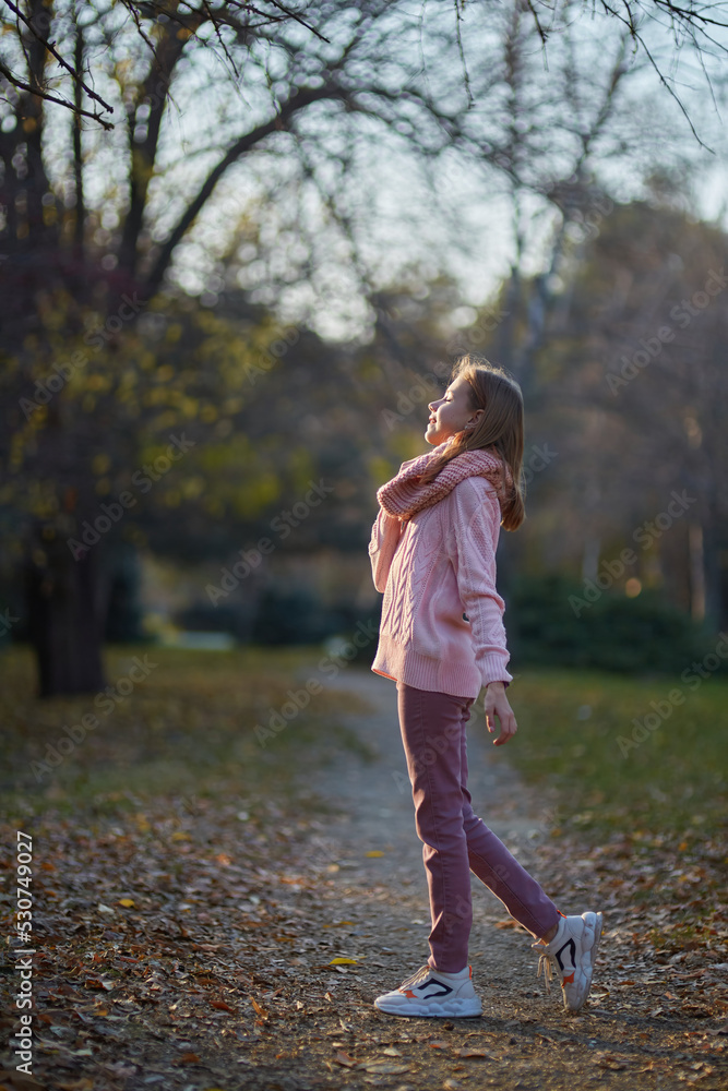 Fototapeta premium A girl in a knitted sweater in an autumn park. September or October, yellow leaves on trees.