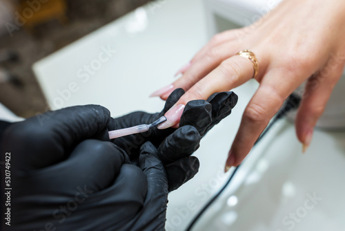 Close-up of a manicurist making a pale pink manicure on a young woman s hand. Manicurist woman doing nails to a client girl in a beauty salon.