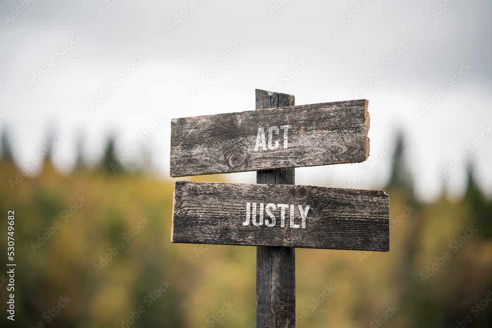 vintage and rustic wooden signpost with the weathered text quote act justly, outdoors in nature. blurred out forest fall colors in the background.