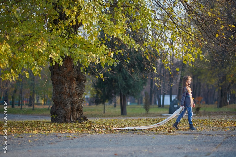 A girl in a knitted sweater in the autumn park is walking along the path. September or October, yellow leaves on trees.