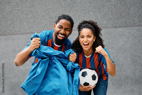 Cheerful black couple cheering for their soccer team and looking at camera. photo