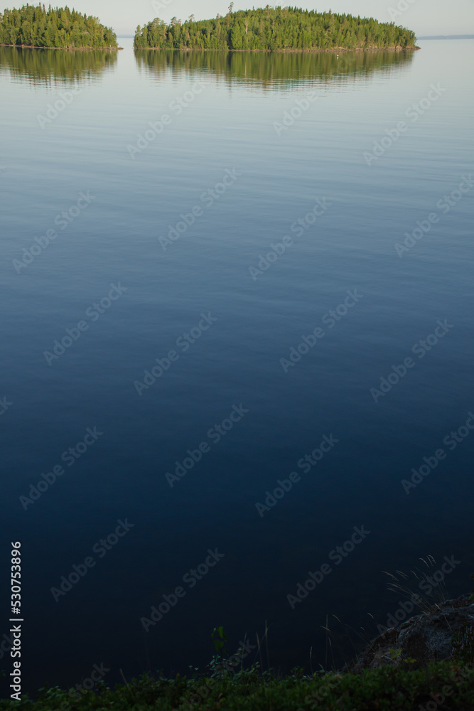 Vertical photo of calm lake water and green islands on the horizon