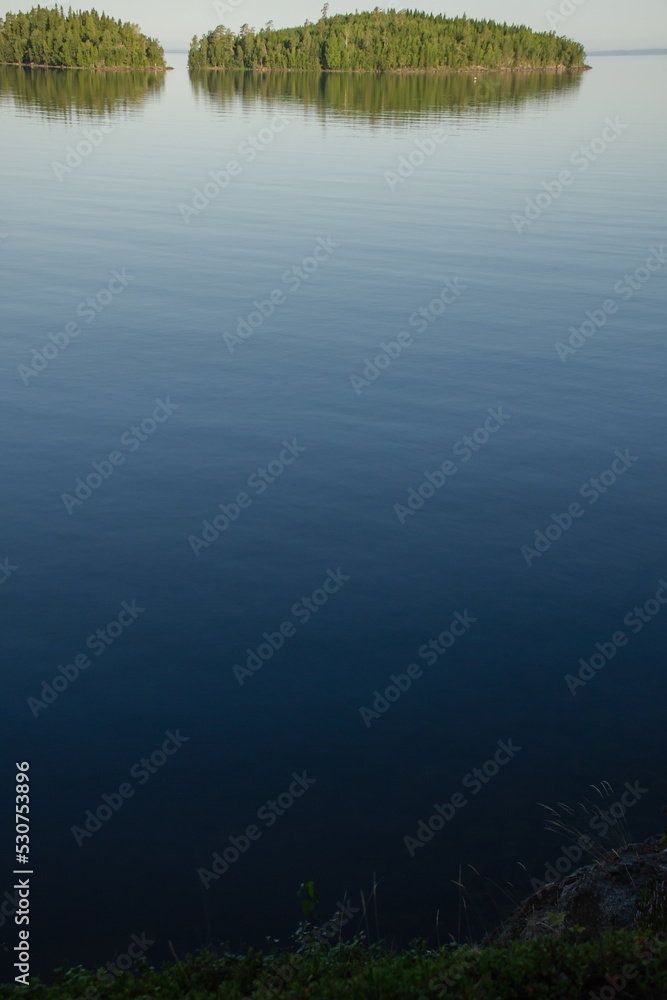 Vertical photo of calm lake water and green islands on the horizon Vertical photo of calm lake water and green islands on the horizon