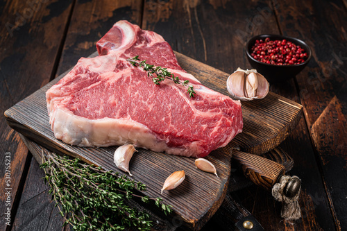 Prime T-bone beef meat steak, raw porterhouse steak on butcher board with herbs. Wooden background. Top view photo