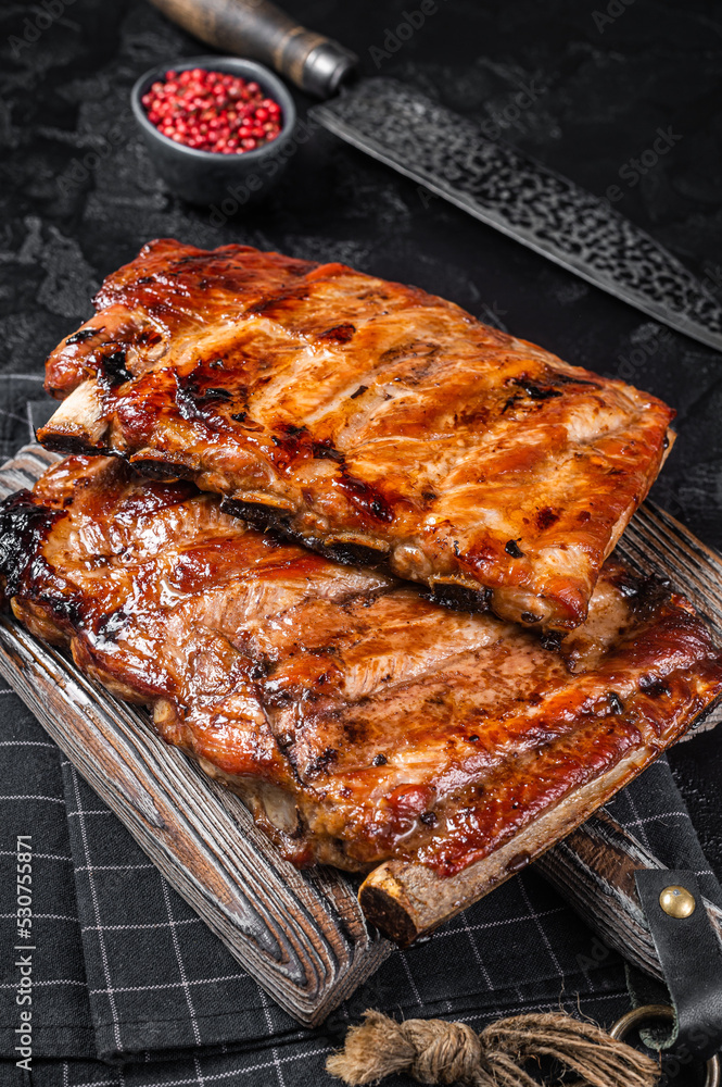 Stack of grilled pork ribs in BBQ sauce on a chopping board. Black background. Top view