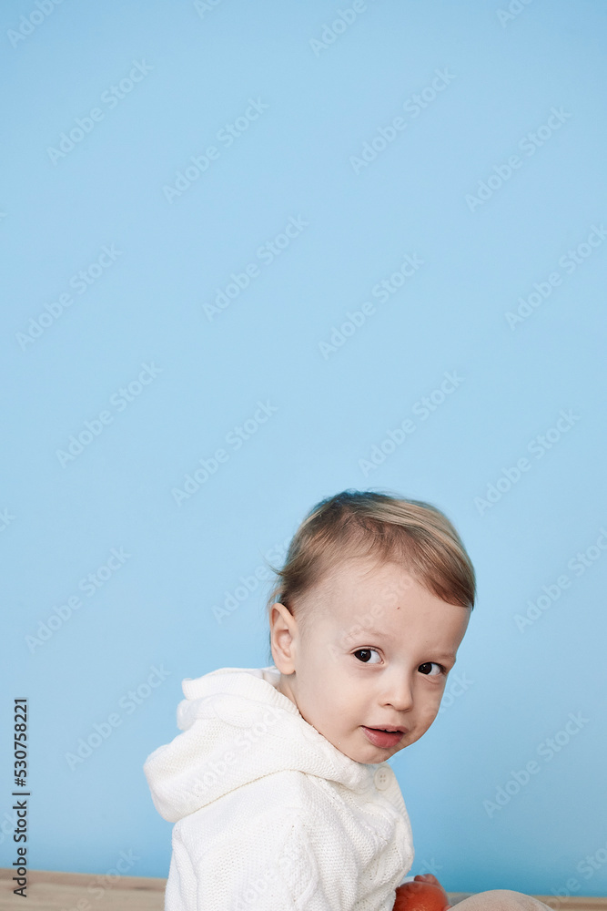 a little boy of 2 years sits in a white jacket on a blue background and thinks laughs happy sad sadness cheerful advertisement for children a little boy of 2 years sits in a white jacket on a blue background and thinks laughs happy sad sadness cheerful advertisement for children