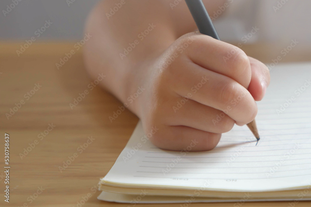 Kid hand writing with pencil in a book on wooden table Kid hand writing with pencil in a book on wooden table