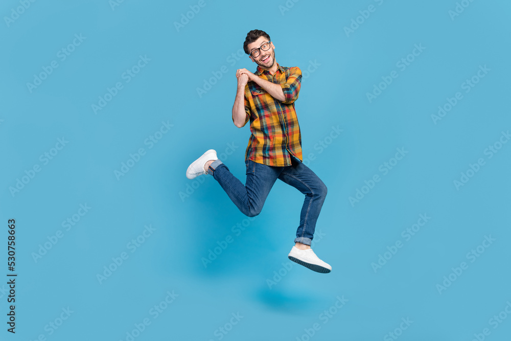 Full length portrait of overjoyed cheerful man jump arms hold empty space isolated on blue color background Full length portrait of overjoyed cheerful man jump arms hold empty space isolated on blue color background