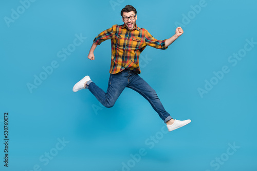 Full size photo of astonished delighted guy jumping raise fists triumph isolated on blue color background