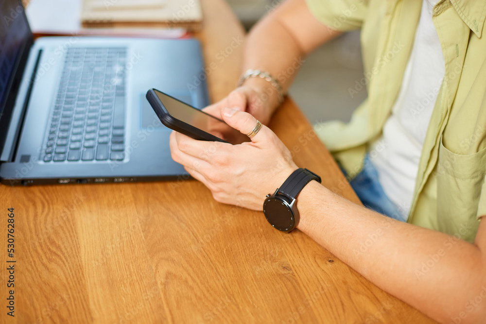 Fototapeta premium Businessman holding smartphone sitting in office, using cell phone mobile apps and laptop