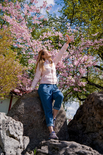 portrait of a smiling blonde woman in spring park in pink blossoming sakura 