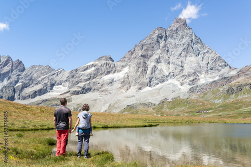 Rear view of a mother carrying her toddler on a baby wrap carrier, joint the father while are looking at Matterhorn during a hiking day at Italian alps. © Esther Pueyo