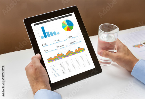 Hands holding a digital tablet with analytical data and a glass of water. photo