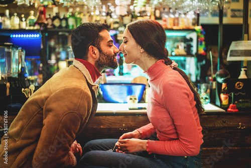 Couple of romantic young people rubbing noses sitting at pub's counter photo