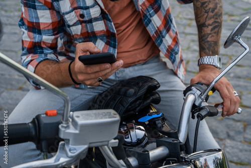 Portrait of trendy guy motorcyclist with smartphone riding motorbike outdoors.