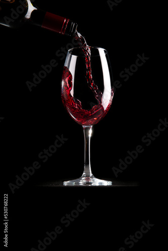 Red wine is poured into a glass on a black background.